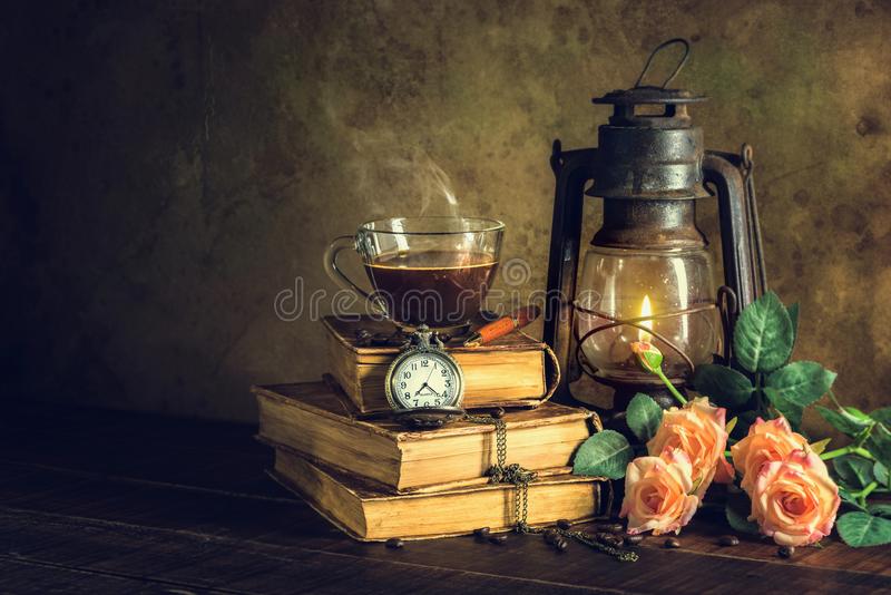 coffee cup glass old books clock vintage kerosene lamp oil lantern burning glow soft light aged wood floor 118213068